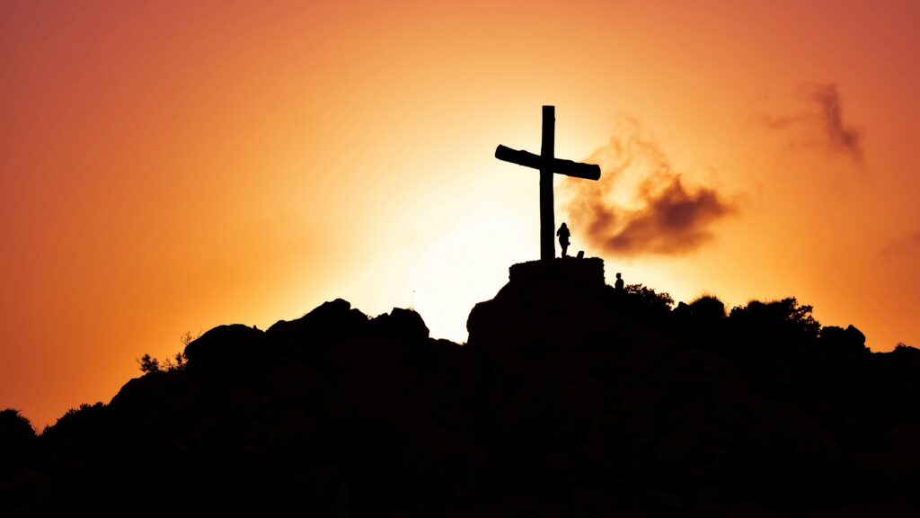 Majestic silhouette of a cross on a hill during a vivid sunset, symbolizing spirituality.